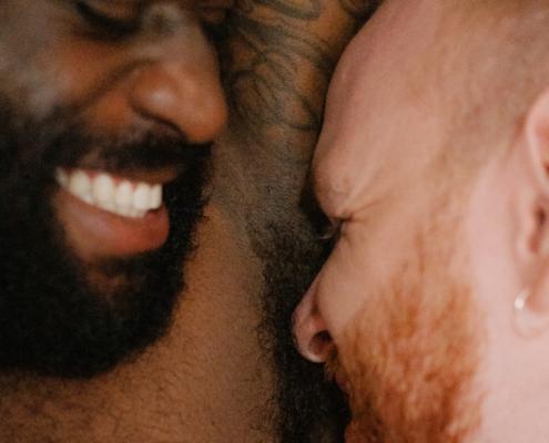 A bisexual man sniffs his smiling partner's armpit