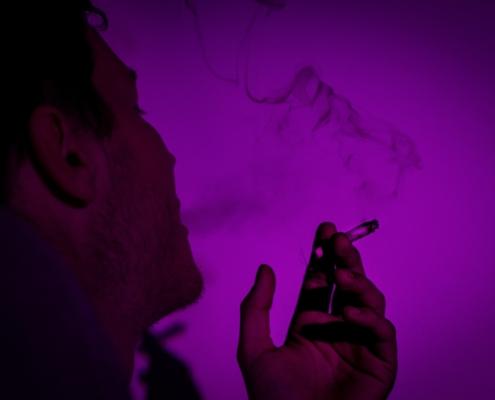 The silhouette of a person smoking against purple light